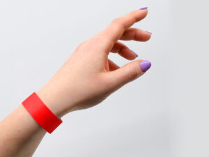 Red Tyvek wristband worn on a wrist. Comfortable and lightweight security band example. Manufacturer AMGS Group.