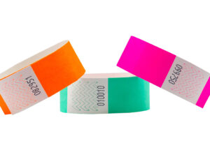 Set of 25mm Tyvek wristbands in orange, green, and pink. Detail view of serial numbering and adhesive zone. Custom Tyvek Wristbands 25 mm. Manufacturer AMGS Group.